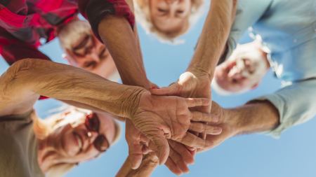 vier Senior*innen stehen im Kreis und geben sich die Hände
