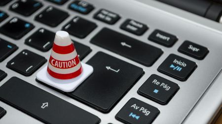 Weißer Warnkegel mit der Aufschrift "Caution" auf einer Laptop-Tastatur