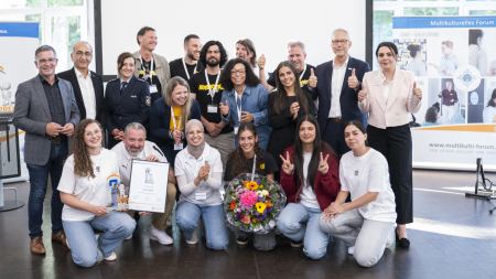 Gruppenfoto: Mehrere Personen halten einen Blumenstrauß, eine Trophäe und eine eingerahmte Urkunde fest.